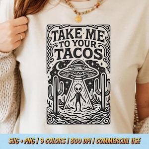 May include: Beige t-shirt featuring a black graphic with the text "TAKE ME TO YOUR TACOS". The design includes a UFO, an alien, and cacti. The shirt is a casual wear item.