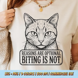 May include: Beige t-shirt featuring a detailed black and white illustration of a cat's face. Below the cat, a rectangular sign reads "REASONS ARE OPTIONAL, BITING IS NOT". The shirt is part of a collection with various color options.