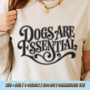 May include: A cream-colored t-shirt with the text "DOGS ARE ESSENTIAL" in a black, vintage-style font. The shirt has a crew neck and short sleeves. The bottom of the image shows text: SVG + PNG | 9 COLORS | 300 DPI | COMMERCIAL USE.