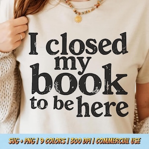 Könnte beinhalten: Beiges T-Shirt mit dem Text "I closed my book to be here" in schwarzer, verwaschener Schrift. Das Shirt hat einen Rundhalsausschnitt. Das Bild zeigt auch eine Halskette.