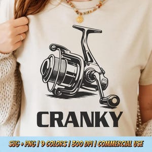 May include: A cream-colored t-shirt featuring a black and white illustration of a fishing reel. Below the reel, the word "CRANKY" is printed in bold, black capital letters. The shirt also includes the text "SVG + PNG | 9 COLORS | 300 DPI | COMMERCIAL USE".