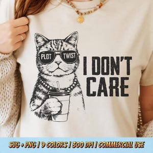 Puede incluir: Camiseta beige con una ilustración en blanco y negro de un gato con gafas de sol con la frase "PLOT TWIST" y sosteniendo una taza de café. El texto "I DON'T CARE" está impreso en el lado derecho.