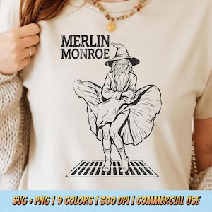 May include: Cream-colored t-shirt featuring a black and white graphic of Merlin Monroe, a wizard in Marilyn Monroe's iconic pose. The text "MERLIN MONROE" is printed above the graphic. The bottom of the shirt has the text "SVG + PNG | 9 COLORS | 300 DPI | COMMERCIAL USE".