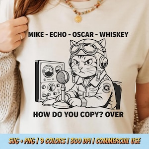 May include: Cream-coloured t-shirt featuring a black and white cartoon of a cat in a pilot's helmet and jacket, operating a microphone and radio. The text above says "MIKE - ECHO - OSCAR - WHISKEY", and below, "HOW DO YOU COPY? OVER".