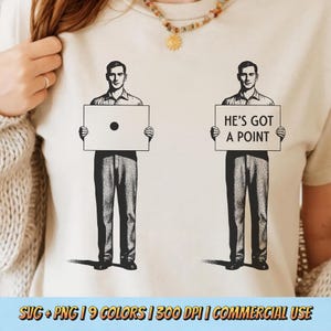 以下が含まれることがあります： ベージュ色のTシャツ。2つの白黒イラストがあり、男性が看板を持っています。1つの看板には黒い点があり、もう1つは「HE'S GOT A POINT」と書かれています。画像の下部には「SVG + PNG | 9 COLORS | 300 DPI | COMMERCIAL USE」と書かれています。