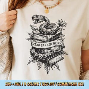 May include: Beige t-shirt featuring a black and white graphic of a snake coiled around a stack of books. A banner across the books reads "Read Banned Books". Leaves and a flower are also included in the design.