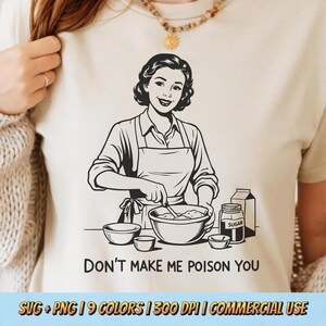 May include: Beige t-shirt with a black and white illustration of a woman cooking, with the text "DON'T MAKE ME POISON YOU". The image includes bowls, a jar of sugar, and a milk carton. The bottom of the shirt has text.