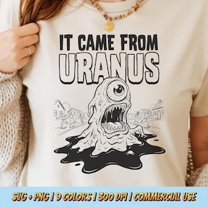 Könnte beinhalten: Beiges T-Shirt mit einem schwarz-weißen Grafikdesign eines einäugigen Monsters und dem Text "IT CAME FROM URANUS". Das Monster hat einen offenen Mund und einen tropfenden Körper. Das Design beinhaltet eine Straßenszene.