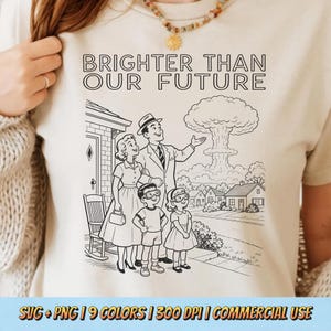 May include: A cream-colored t-shirt featuring a black line-art illustration of a family standing outside a house, looking at a mushroom cloud in the distance. The text above the illustration reads BRIGHTER THAN OUR FUTURE in a bold, sans-serif font.