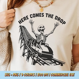 May include: Beige t-shirt with a black graphic of a skeleton riding a roller coaster. The text "HERE COMES THE DROP" is above the skeleton. The bottom of the shirt has the text "SVG + PNG | 9 COLORS | 300 DPI | COMMERCIAL USE."