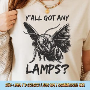May include: Cream-colored t-shirt featuring a detailed black and white illustration of a moth with the text "Y'ALL GOT ANY LAMPS?". The shirt also includes the text "SVG + PNG | 9 COLORS | 300 DPI | COMMERCIAL USE".
