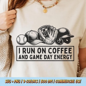 May include: A beige t-shirt with a baseball, cap, glove, and helmet graphic. The text "I RUN ON COFFEE AND GAME DAY ENERGY" is in a black box. The shirt is a neutral colour, suitable for casual wear.