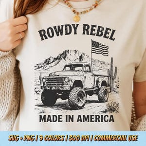 May include: Cream-colored t-shirt featuring a black and white graphic of a vintage truck with an American flag and desert landscape. Text reads "ROWDY REBEL" and "MADE IN AMERICA".