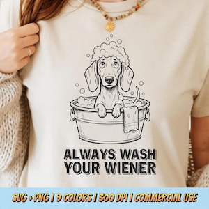 Puede incluir: Camiseta beige con una ilustración en blanco y negro de un perro salchicha en una bañera con burbujas. El texto "ALWAYS WASH YOUR WIENER" está debajo. La camiseta tiene cuello redondo.