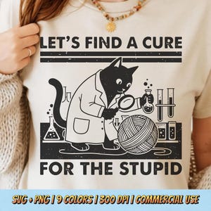 May include: Beige t-shirt with a black graphic of a cat in a lab coat examining a ball of yarn with a magnifying glass. Text reads "LET'S FIND A CURE FOR THE STUPID". Below the text are the words "SVG + PNG | 9 COLORS | 300 DPI | COMMERCIAL USE".