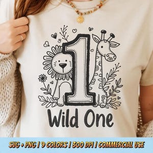 Może przedstawiać: Beżowa koszulka z czarno-białą grafiką na pierwsze urodziny. Projekt zawiera dużą cyfrę "1" z lwem i żyrafą, otoczoną liśćmi i sercami. Poniżej znajduje się napis "Wild One".