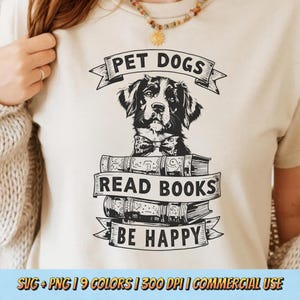 May include: Cream-colored t-shirt with a black and white graphic of a dog wearing a bow tie, atop a stack of books. The text reads "PET DOGS READ BOOKS BE HAPPY". The shirt is a casual wear item.