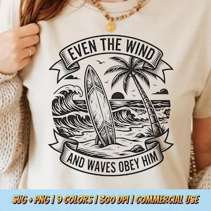May include: A cream-coloured t-shirt with a black and white graphic depicting a surfboard on a beach with waves, a palm tree, and the text "EVEN THE WIND AND WAVES OBEY HIM". The design includes a banner and a sunset.