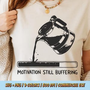Puede incluir: Camiseta beige con un gráfico negro de una cafetera vertiendo en una barra de progreso, con el texto "MOTIVATION STILL BUFFERING". Una prenda de vestir casual.