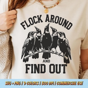 May include: Cream-colored t-shirt featuring a graphic of five black crows perched on a branch. The text "FLOCK AROUND AND FIND OUT" is printed above and below the birds in bold, black letters. The shirt is a casual wear item.