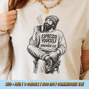Peut inclure: Un t-shirt couleur crème avec une illustration graphique noire représentant une personne barbue portant un bonnet, assise sur un tabouret et buvant dans une tasse. Le texte indique ESPRESSO YOURSELF SOMEWHERE ELSE sur la poitrine.