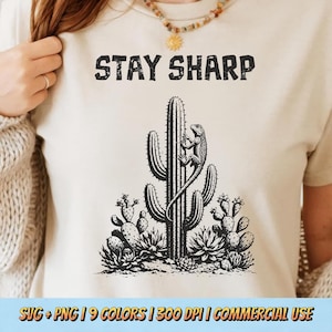 Puede incluir: Camiseta color crema con una ilustración en blanco y negro de un cactus y un lagarto. El texto "STAY SHARP" está impreso encima del cactus. La parte inferior de la camiseta tiene el texto "SVG + PNG | 9 COLORS | 300 DPI | COMMERCIAL USE".