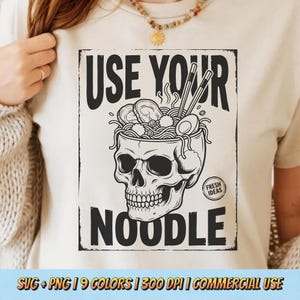 May include: Beige t-shirt with a black graphic of a skull bowl filled with ramen, chopsticks, and the text "USE YOUR NOODLE." The design includes the words "FRESH IDEAS" and is a unique, food-themed design.
