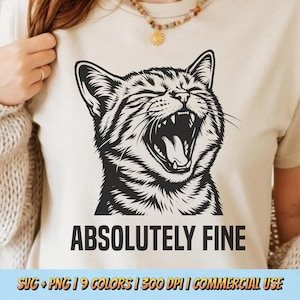 May include: A cream-colored t-shirt featuring a black and white illustration of a yawning cat with the text "ABSOLUTELY FINE" below. The shirt has a crew neck and short sleeves. The bottom of the image includes text about the design's availability in multiple colors and its commercial use.