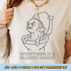 May include: A cream-coloured t-shirt featuring a black line art graphic of a fish with an angry expression sitting inside a toilet bowl. Below the graphic, the text reads: EVERYTHING IS A HILARIOUS TRAGEDY. The shirt has a crew neckline.