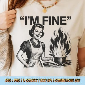 May include: Beige t-shirt with the phrase "I'M FINE" in black. The graphic depicts a vintage illustration of a woman in an apron smiling while a pot on a stove is on fire. The bottom of the shirt has text.