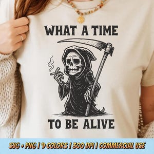 May include: Beige t-shirt featuring a black graphic of the Grim Reaper smoking a cigarette and holding a scythe. The text "WHAT A TIME TO BE ALIVE" is above and below the illustration.