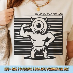 May include: Beige t-shirt with a black and white illustration of a muscular cyclops and the text "I HAVE MY EYE ON YOU". The cyclops has one large eye, horns, and a toothy grin. The shirt also includes the text "SVG + PNG | 9 COLORS | 300 DPI | COMMERCIAL USE".