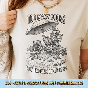 Peut inclure: T-shirt beige avec un dessin en noir et blanc d'un squelette lisant sur une plage, sous un parasol. Le texte indique "TOO MANY BOOKS" et "NOT ENOUGH LIFETIMES".