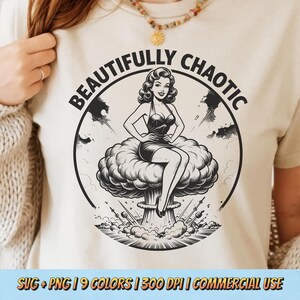 May include: Beige t-shirt featuring a black and white graphic of a woman sitting on a mushroom cloud, encircled by the words "BEAUTIFULLY CHAOTIC". The design is a retro-style illustration.