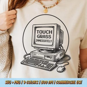 Pode incluir: Camiseta bege com um gráfico a preto e branco de um computador retro. O ecrã mostra "TOUCH GRASS IMMEDIATELY". O design inclui um teclado e um rato, tudo dentro de um círculo preto.