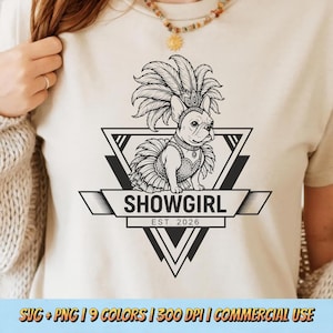 May include: A cream-coloured t-shirt with a black and white graphic of a French Bulldog in a showgirl outfit, including a feathered headdress and tutu. The text "SHOWGIRL EST. 2026" is below the dog within a geometric design.