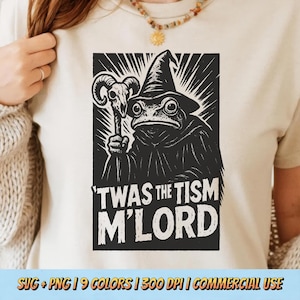 Puede incluir: Camiseta color crema con un gráfico en blanco y negro de una rana vestida de mago, sosteniendo un bastón con una calavera. El texto "'TWAS THE TISM M'LORD" está debajo. La parte inferior de la camiseta tiene el texto "SVG + PNG | 9 COLORS | 300 DPI | COMMERCIAL USE".