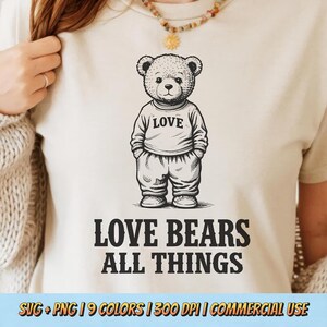 May include: A cream-colored t-shirt featuring a black and white illustration of a teddy bear wearing a sweater with the word "LOVE". Below the bear, the text reads "LOVE BEARS ALL THINGS".