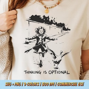 Puede incluir: Camiseta beige con una ilustración en blanco y negro de un niño corriendo con un ganso. El texto "THINKING IS OPTIONAL" está impreso debajo. La camiseta es de color neutro claro.