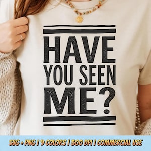 May include: A cream-colored t-shirt with the text "HAVE YOU SEEN ME?" in bold, black letters. The text is centered and framed by horizontal black lines. The shirt is part of a clothing collection.