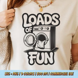 May include: A cream-colored t-shirt featuring a black and white graphic of a washing machine with the text "LOADS OF FUN". The washing machine has an open door with a towel inside. Below the graphic are the words "SVG + PNG | 9 COLORS | 300 DPI | COMMERCIAL USE".