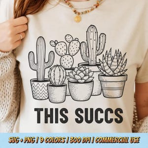 May include: Beige t-shirt featuring a black and white illustration of various potted cacti and succulents. Below the image, the text reads "THIS SUCCS". The shirt is a neutral color and suitable for casual wear.