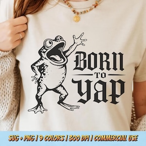 Può includere: T-shirt color crema con un'illustrazione di una rana nera dei cartoni animati, con la bocca aperta e un braccio alzato. Il testo "BORN TO YAP" è stampato in un carattere gotico sotto la rana. La parte inferiore della maglietta ha il testo "SVG + PNG | 9 COLORS | 300 DPI | COMMERCIAL USE".