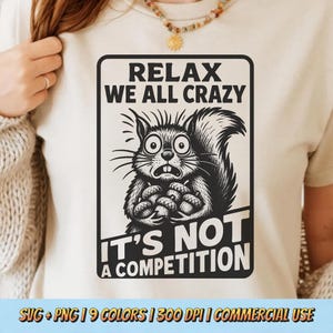 May include: A cream-colored t-shirt featuring a black and white graphic of a startled squirrel clutching acorns. The text "RELAX WE ALL CRAZY IT'S NOT A COMPETITION" is above and below the squirrel illustration. The bottom of the shirt has text that reads "SVG + PNG | 9 COLORS | 300 DPI | COMMERCIAL USE".