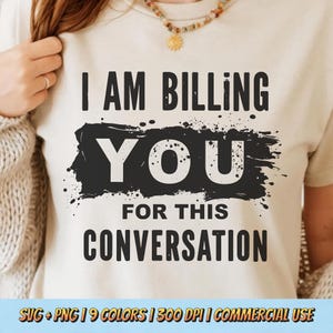 May include: A beige t-shirt with the text "I AM BILLING YOU FOR THIS CONVERSATION" in black. The word "YOU" is in a white font on a black splatter background. The shirt is being worn by a person.