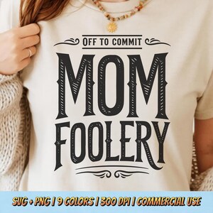 May include: A cream-colored t-shirt with the text "OFF TO COMMIT MOM FOOLERY" in black, stylized lettering. The shirt is being worn by a person. The shirt also has the text "SVG + PNG | 9 COLORS | 300 DPI | COMMERCIAL USE".