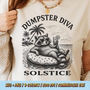 Peut inclure: Un t-shirt couleur crème avec un motif noir représentant un raton laveur portant des lunettes de soleil en forme de cœur, allongé sur une bouée en forme de beignet dans l'océan. Le texte indique DUMPSTER DIVA SOLSTICE. Un palmier est visible.