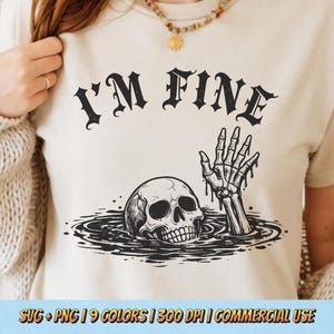 Puede incluir: Camiseta beige con la frase "I'M FINE" en fuente gótica negra. Debajo, un gráfico de una calavera y una mano esquelética emergiendo del agua. El diseño tiene un tema espeluznante de Halloween.
