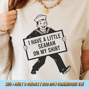 Può includere: Una maglietta color crema con un'illustrazione in bianco e nero di un marinaio che tiene in mano un cartello. Il cartello dice "I HAVE A LITTLE SEAMAN ON MY SHIRT". Il marinaio sorride e indossa un cappello da marinaio.