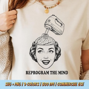 Op de afbeelding: Beige t-shirt met een zwart-witte afbeelding van een vrouwenhoofd met een open bovenkant, waar een hersen wordt gemixt door een mixer. De tekst "REPROGRAM THE MIND" staat onder de afbeelding.